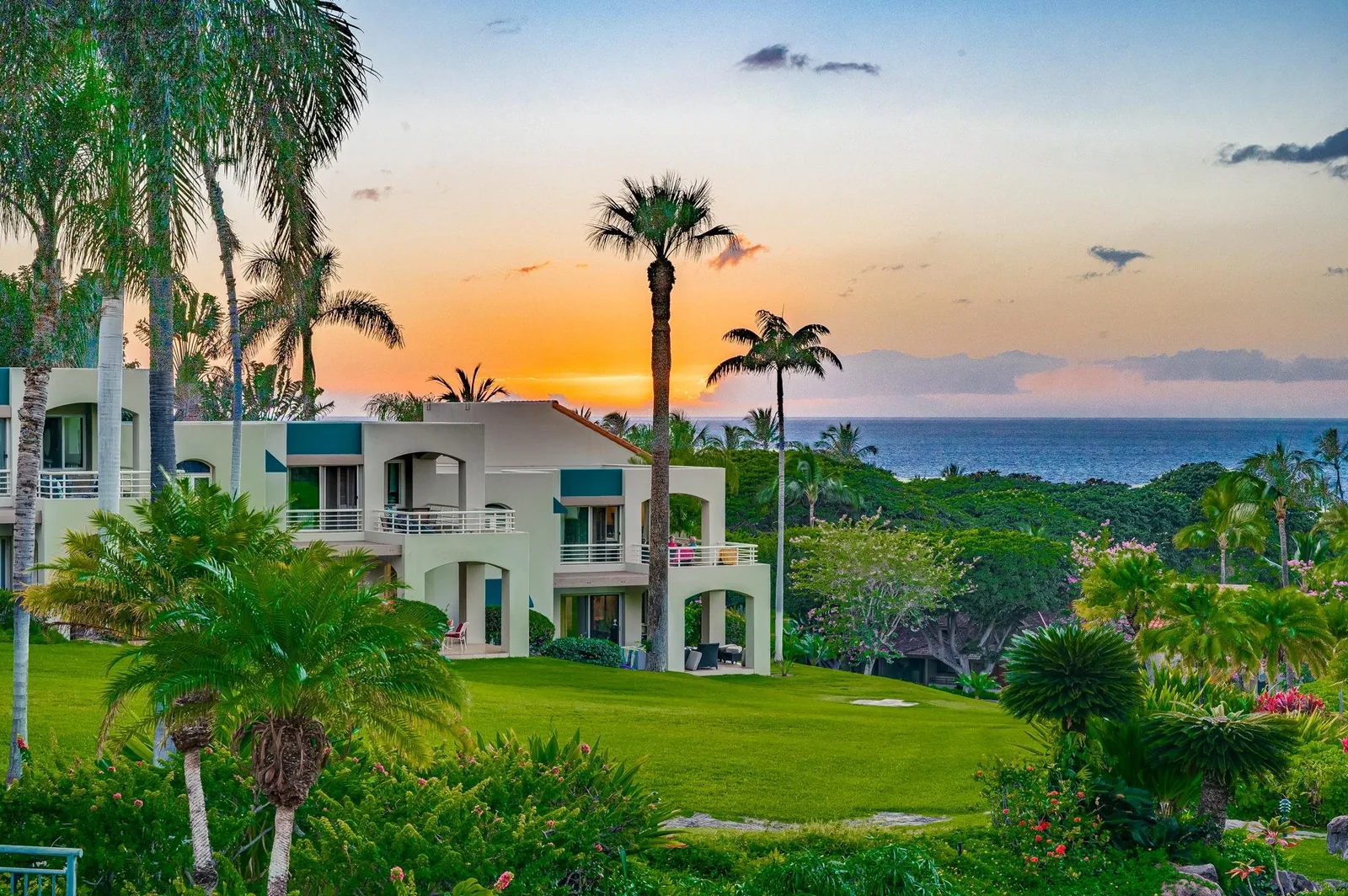 A Wailea residence at golden hour with a manicured lawn, palms and an ocean view under an orange sky