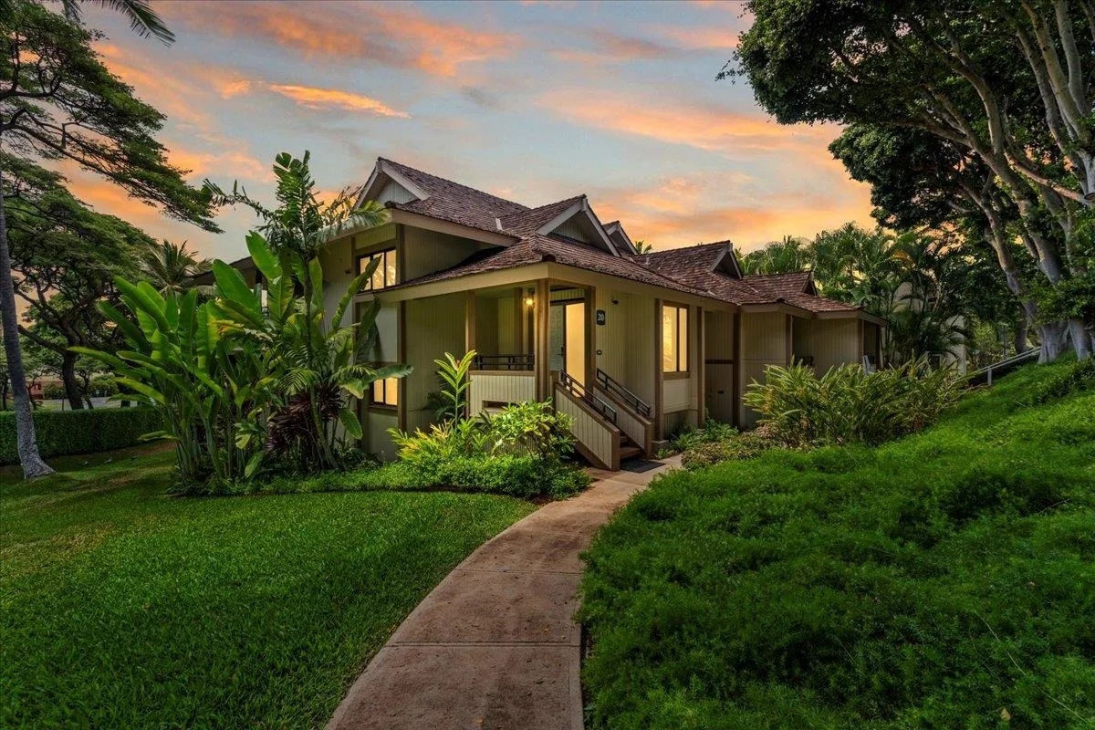A plantation-style Wailea cottage with a shingle roof and lush tropical landscaping at dusk